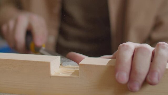 Close up shot of hands of unrecognizable woodworker cutting mortise in wooden plank with chisel