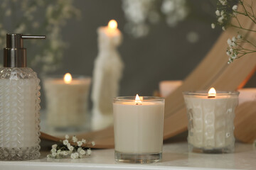 Fototapeta na wymiar Beautiful burning candles and gypsophila flowers on white table near mirror indoors.