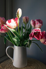 Pink tulip flower bouquet with green fresh stems in a white porcelain jar vase on a white window frame with blue sky background. Vibrant colourful botany floral home decor idea.