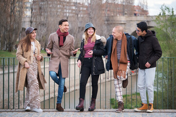 Group of five friends of different ages and ethnicities talking and laughing outdoors in winter.
