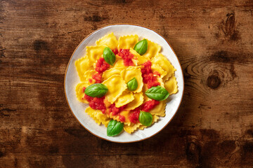 Italian ravioli with red tomato sauce and basil, overhead shot on a dark rustic wooden background