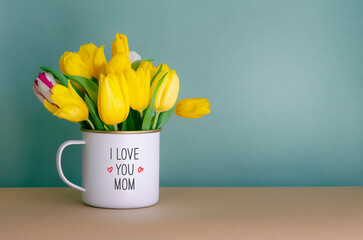 Happy Mother's Day greeting card. Bouquet of fresh yellow tulips in a white mug on a dark turquoise...