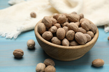 Bowl with nutmeg seeds on light blue wooden table, closeup