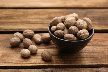 Bowl with nutmeg seeds on wooden table, closeup. Space for text