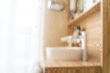 Water drops on wet glass shower door in hotel bathroom with blured bokeh window, sink, faucet and...