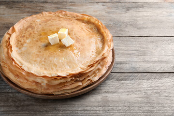 Stack of delicious crepes with melting butter on wooden table. Space for text
