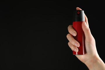 Woman holding pepper spray on black background, closeup. Space for text