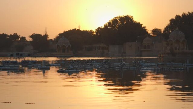 View of the Gadisar Lake during sunset with chhatri in the middle of the lake  at Jaisalmer in Rajasthan, India. Reflection of the Chhatri pavilion in the orange water of the lake during sunset.