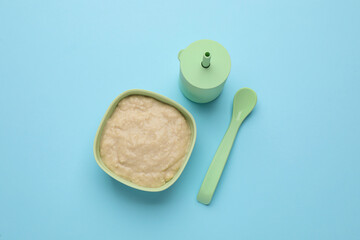 Fototapeta na wymiar Healthy baby food in bowl and bottle with drink on light blue background, flat lay