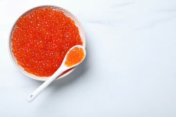 Bowl and spoon with delicious red caviar on white table, top view. Space for text