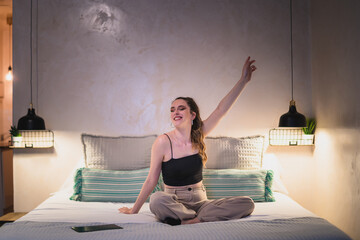 Chica joven sonriendo feliz sobre la cama de un hotel mientras viaja