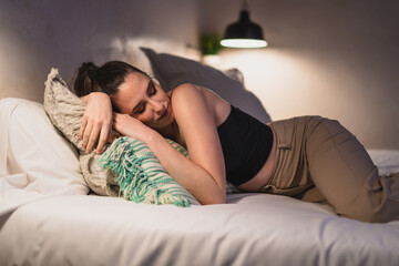 Naklejka premium Chica joven delgada tumbada de lado sobre cama de hotel mientras descansa y mira el smartphone