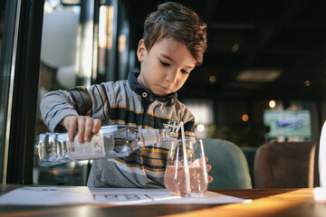 A little boy pours himself a glass of water from a bottle in a cafe. Independence and maturity. High quality photo