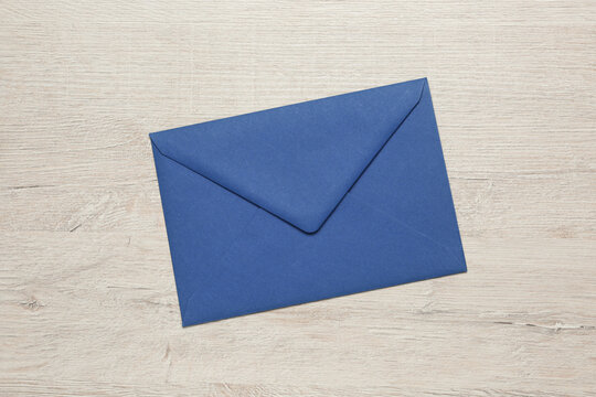 Blue envelope on white wooden table, top view