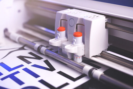 cutting plotter machine with adjustable blades makes adhesive lettering from black vinyl foil in bright light with blue highlights. selective focus. advertising concept