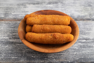 Heap of cheese sticks on a wooden plate on a gray. Side view.