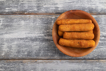 Heap of cheese sticks on a wooden plate on a gray. Top view, copy space.