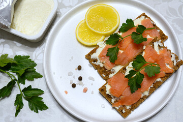crispbread with soft cheese, salmon slices and parsley on white plate with lemon slices and allspice