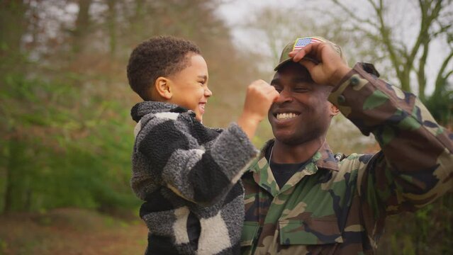 American soldier coming home on leave with son trying on his army uniform cap outdoors - shot in slow motion