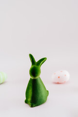 Green bunny rabbit figurine and colored easter eggs in different patterns on neutral pink...