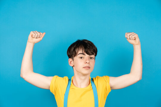 Slim teenager boy showing his biceps muscles. Arrogant adolescent on blue background. Flag colors of Ukrania