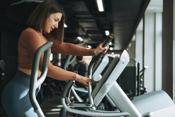 Young fitness brunette woman training for cardio equipment at gym