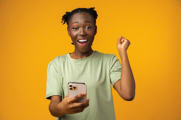 Happy smiling african american girl using her smartphone in yellow studio.