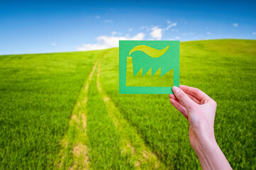 Hand holds green lidustry symbol on nature background.