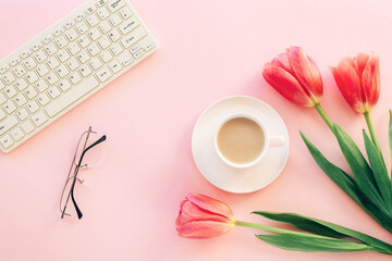 Pink female workplace with keyboard, tulip flowers, coffee cup and glasses. Spring holidays, mothers day concept. Top view, flat lay