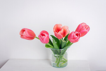 Bouquet of pink tulips in glass vase on white table. Spring holidays concept. Close up