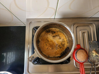 Stock photo of boiling special Indian style masala tea in the steel container, tea stainer kept on gas stove in the kitchen. Picture captured under natural light at Bangalore, Karnataka, India.