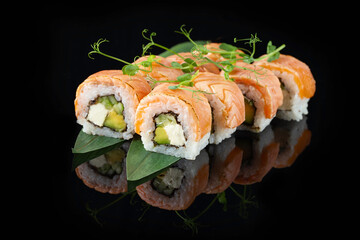 Traditional delicious fresh sushi roll set on a black background with reflection. Sushi roll with rice, nori, cream cheese, tobiko caviar, avocado. Sushi menu. Japanese kitchen. Asian food
