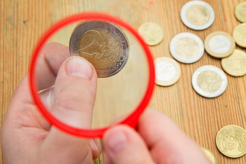 Euro coins magnified by hand magnifier. The young man holds a magnifying glass over the coins. The...