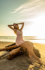 Fototapeta na wymiar Young Bohemian girl posing on driftwood at sunset