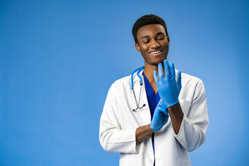 Young African American doctor putting on surgical gloves on blue background
