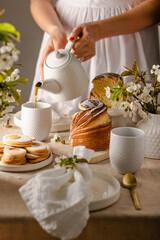 Happy easter. Woman pouring tea. Traditional Easter cake , homemade kraffin with raisins, candied fruits .Cherry blossom on white background. Selective focus. Close up of homemade Cruffin.