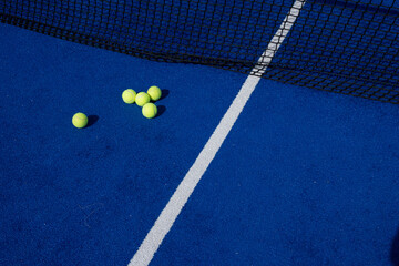 five paddle tennis balls and the net of a blue paddle tennis court, selective focus