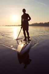 River landscape with silhouette of a man paddle on stand up paddle boarding (SUP) at sunrise on...