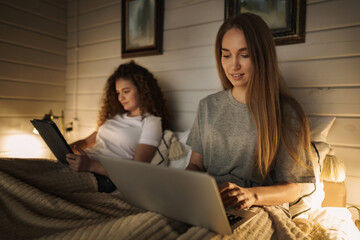 Two beautiful women lying in bed, holding a laptop