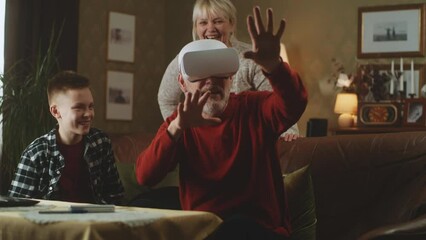 In the living room a teenage grandson and a grandmother are watching grandfather in modern augmented reality glasses - Powered by Adobe