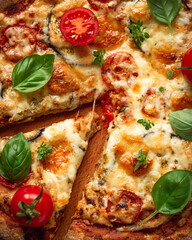 Vegetarian pizza with addition eggplants, cherry tomatoes and aromatic basil herbs, divided into portions on a wooden background, top view