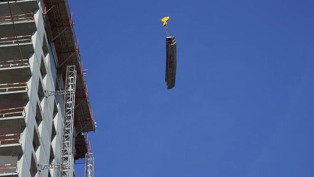 Raise building load to height. Crane lowers loads at construction site. Work process. Crane lifts materials on roof for construction decoration. raised telescopic boom on site. sling hoist crane arm