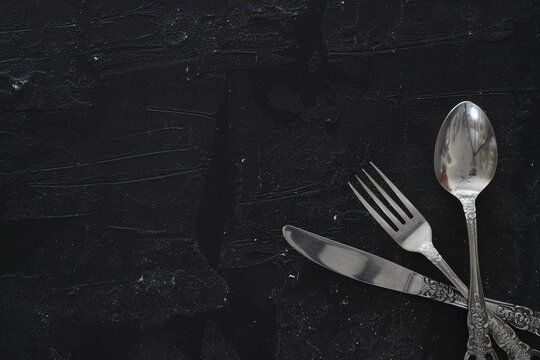 Overhead shot of silverware on black table with copy space.