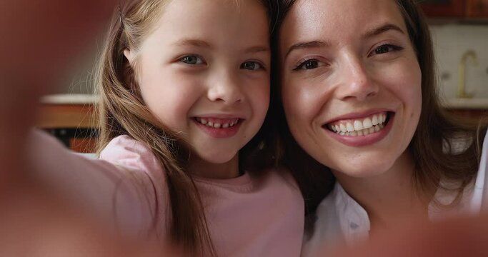 Close up beautiful faces young mom her little daughter having wide toothy smile staring at cam, view through joined fingers showing heart sign. I Love You, happy motherhood, dental services ad concept
