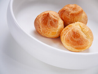 Fresh made profiterole cakes on a white plate. Copy space. Close-up. Selective focus. Horizontal. High key. White background. Diagonal composition.