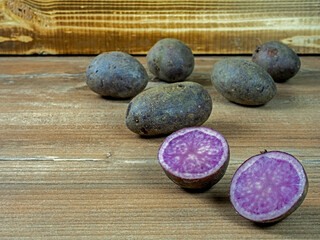 Mehrere Kartoffeln der lilafarbenen Sorte Violetta auf Holz vor einer Holzkiste, eine Kartoffel angeschnitten