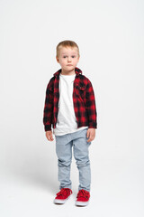 Little boy in red shirt and blue trousers, standing on a white background in studio - preschool kid