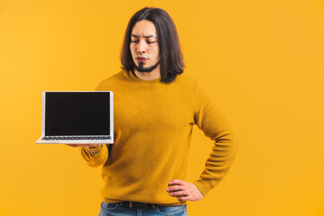 Angry caucasian bearded man with long hair looking at his laptop with mock-up black screen. Copy space studio shot over yellow background. High quality photo