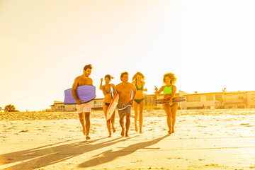 Friends in swimwear running carrying bodyboards on beach