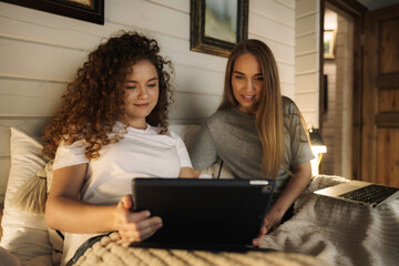 Two beautiful women lying in bed, holding a laptop